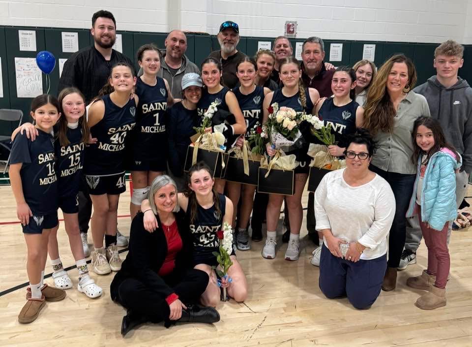 Young women in blue basketball uniforms holding flowers and pictured with some adults